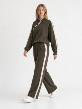 Model wearing an olive-green tracksuit with white side stripes and white sneakers, walking forward.