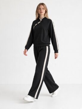 Model wearing a black tracksuit with white side stripes on the sleeves and pants, paired with white sneakers.