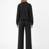 Back view of a person wearing a black tracksuit with beige side stripes on sleeves and pants.